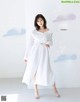 A woman in a white dress standing in front of a white wall.