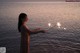 A woman holding a sparkler in front of the ocean.