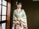 A woman in a green and pink kimono standing in front of a window.