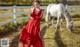 a woman in a red dress standing next to a white horse